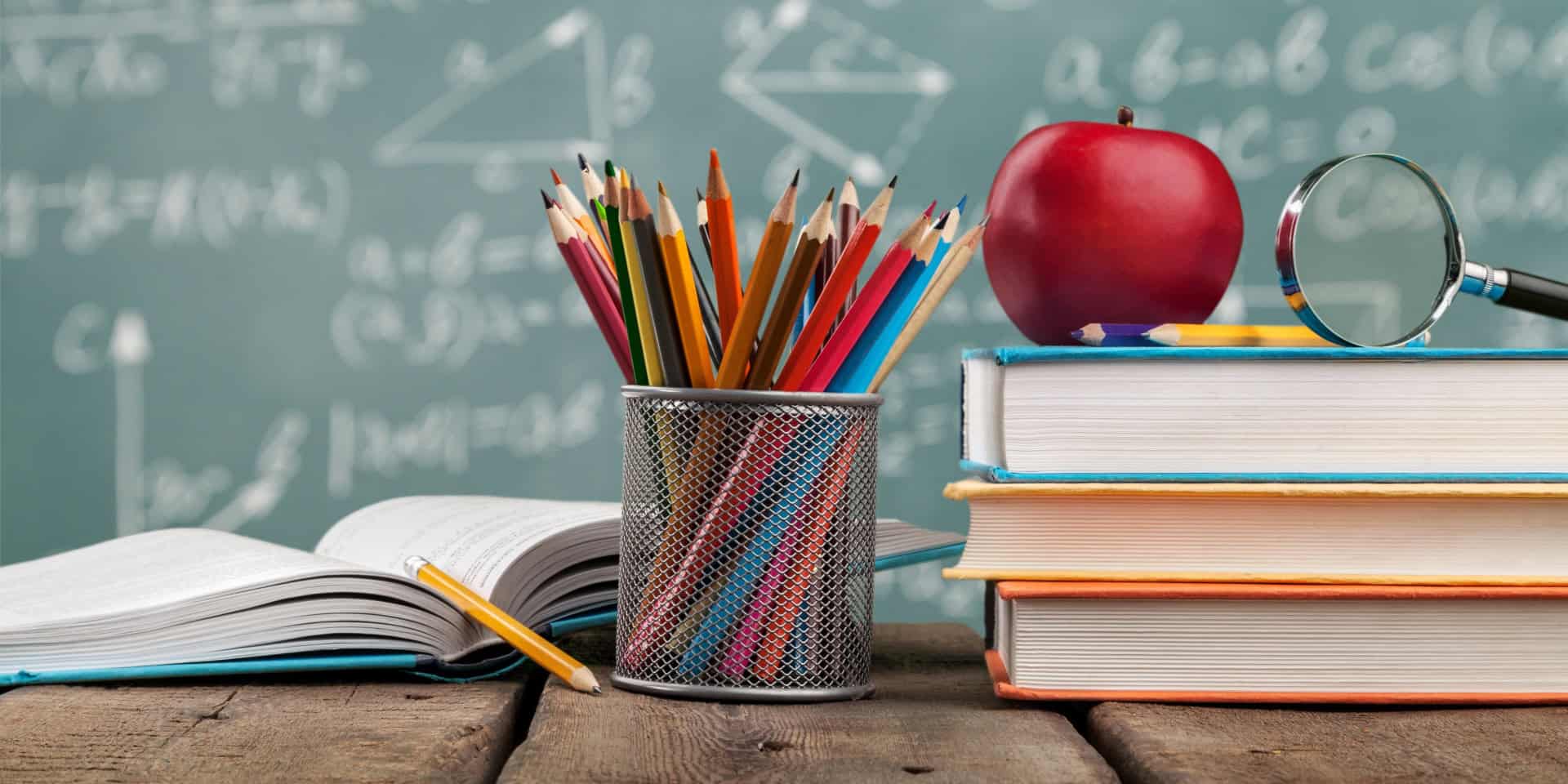 A desk with books, pencils, and a magnifying glass with a chalkboard in the background.